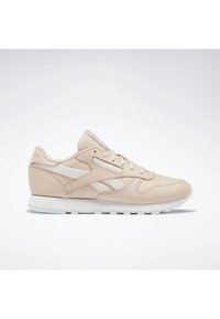 Baskets basses beige Reebok avec semelle blanche, design à lacets et logo bande latérale blanche sur fond clair uni.