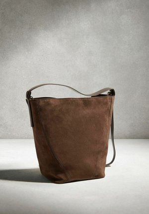 Ruda zomšinė kibirinė rankinė su vienu petnešos dirželiu, padėta ant neutralios pilkos ir baltos spalvų fono.