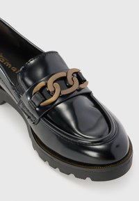 Black patent leather loafer with a raised block heel, featuring a gold-tone chain detail across the instep and textured black rubber sole.