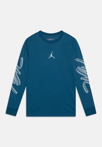Teal pitkähihaisessa paidassa, joka on valmistettu puuvillasta, on keskellä valkoinen Jordan-logo ja abstrakteja valkoisia kuvioita molemmissa hihoissa. Pyöreä kaula-aukko.