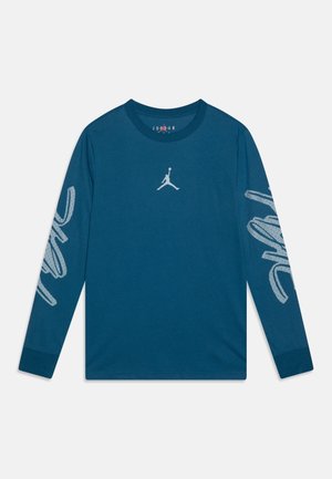 Tyrkysová dlouhá rukávová košile vyrobená z bavlny, se středovým bílým logem Jordan a abstraktními bílými vzory na obou rukávech. Design s kulatým výstřihem.
