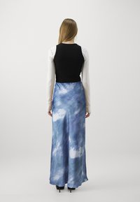 Mustapaita ilman hiuksia valkoisen pitkähihaisen paidan päällä, yhdistettynä siniseen siti-painettuun maksihameeseen. Helma koskettaa maata, sileä kangas.