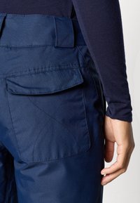 Tengerészkék nadrág texturált felülettel, hátsó zsebbel és látható varrási részletekkel. Az anyag tartósnak és vízállónak tűnik.