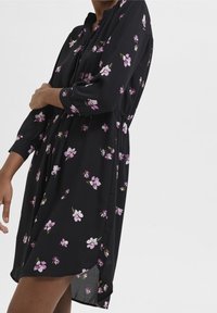 Vestido negro con estampado floral en tonos de rosa y blanco, que cuenta con un diseño de botones, mangas tres cuartos y una cintura fruncida.