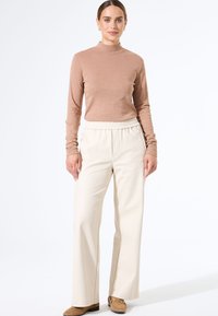 Langsleeve top in roségoud met een opstaande kraag, gecombineerd met crèmekleurige, wijde broekspijpen met een elastieken taille en zijzakken.