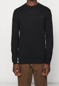 Suéter negro de manga larga con cuello redondo y un pequeño logo bordado en el pecho. Fabricado con tejido de punto suave.