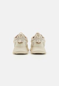 Baskets beige avec une tige en maille et en synthétique, semelle en caoutchouc, et col de cheville rembourré avec une boucle pour un ajustement facile.