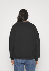 Czarna, oversized bluza z miękkiego materiału, z opadającymi ramionami, ribbami przy mankietach i okrągłym dekoltem. W połączeniu z niebieskimi dżinsami.