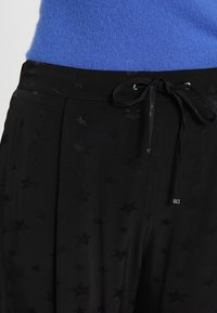 Svarta byxor med ett stjärnmönster, med en texturerad yta, dragsko i midjan och en slät finish. Försedda med silverdetaljer.