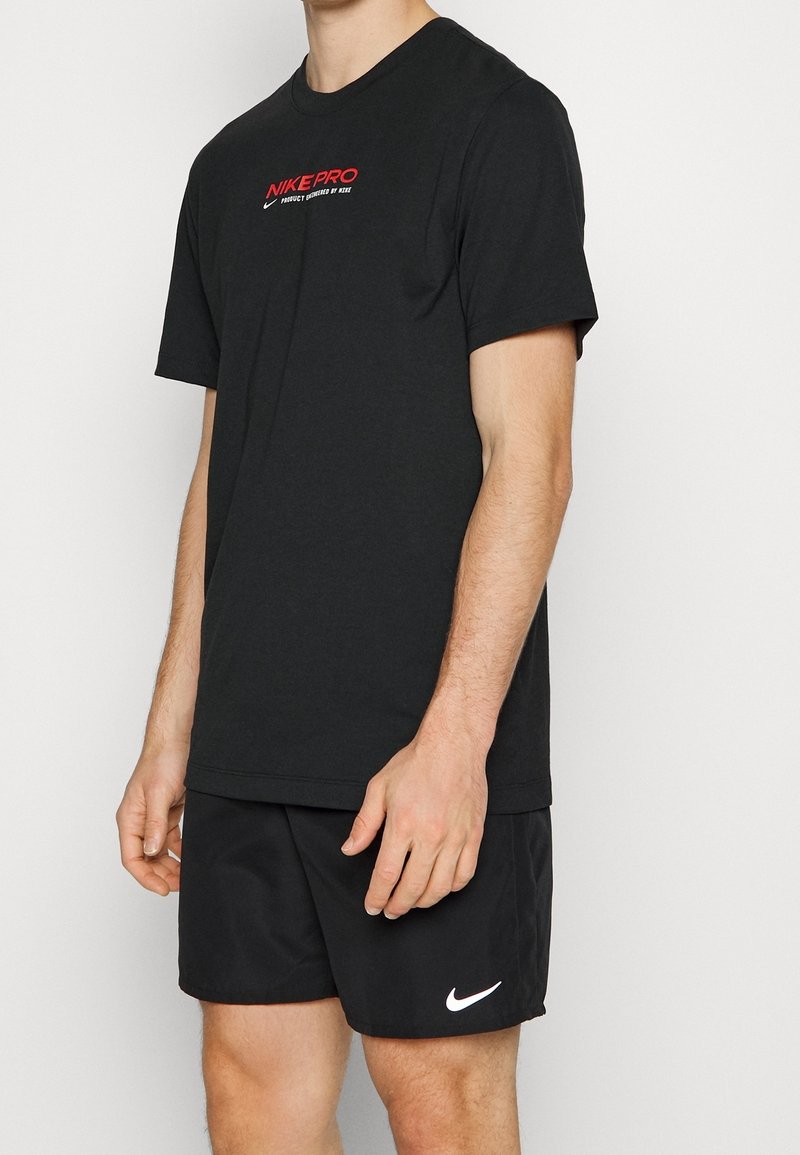 Musta Nike Pro t-paita lyhyillä hihoilla ja punaisella logolla rinnassa, yhdistettynä mustiin shortseihin, joissa on valkoinen Nike swoosh. Sileä kangastuntuma.