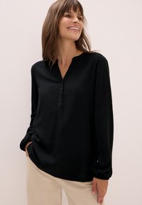 Schwarze langärmlige Bluse mit V-Ausschnitt und geknöpfter Blende, aus glattem Stoff. Mit gerafften Ärmelbündchen und lockerer Passform.