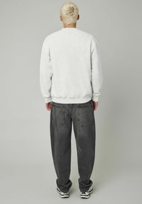 Sweat-shirt gris clair avec des poignets et un ourlet côtelés, associé à un jean noir gris ample avec des poches arrière et des ourlets retroussés.