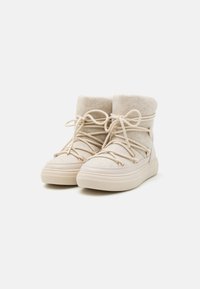 Bottes chelsea beiges avec une tige en tissu texturé, bout rond et col en polaire doux. Lacets maintenus avec des accents en métal rose.