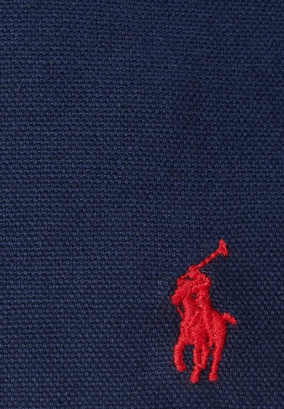 Jūras spēku krāsas teksturēts audums ar izteiktu sarkanu izšūtu polo spēlētāja logo, kas novietots labajā apakšējā stūrī.
