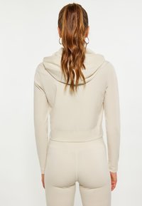 Felpa corta beige con un ampio cappuccio e design aderente. Tessuto morbido e liscio con una leggermente elasticità e cuciture minime.