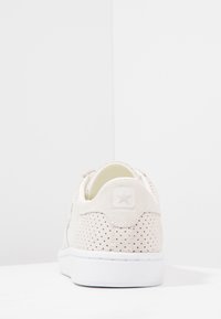 Beige perforerade mockasinsneakers med rundad baksidan, vit sula och stjärnlogotyp på häl. Slät textur med minimalistisk design.