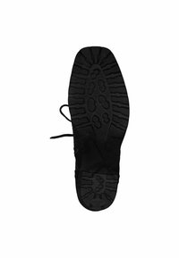 Semelle de chaussure de sport noire avec caoutchouc texturé. Présente un motif de semelle distinct et des détails de laçage. La partie inférieure est lisse avec des rainures pour la traction.