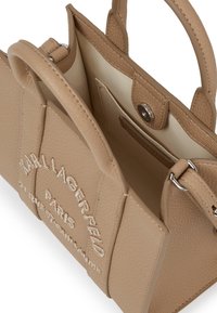 Beżowa torba skórzana o fakturze z otworem górnym, szczegółami logo i kieszenią wewnętrzną. Posiada podwójne, krótkie uchwyty oraz srebrne okucia.