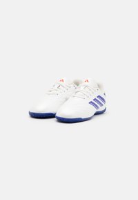 Zapatillas de fútbol blancas con rayas moradas, suela de goma, parte superior de cuero suave y lengüeta de malla ventilada. Presenta acentos de logo rojo.
