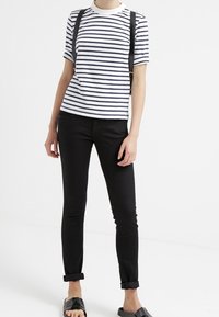 Pruhované tričko s krátkým rukávem v bílé a námořnické modři, v kombinaci s černými skinny džíny. Tričko má kulatý výstřih a ramínka.