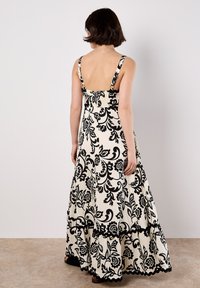 Robe maxi avec un motif floral noir et blanc, dos froncé, bretelles ajustables et ourlet en dentelle, fabriquée en tissu léger.