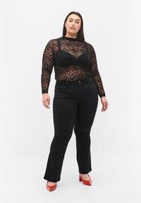 Top de encaje negro de manga larga superpuesto sobre un sujetador negro, combinado con unos pantalones de mezclilla negros acampanados y zapatos de tacón cuadrado rojos. Texturas suaves y patrones intrincados.