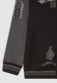 Czarny i szary sweter z nadrukowanym numerem "8", grafiką piankowego palca "#1" oraz banerem "CHAMPION". Posiada paskowe mankiety i kieszeń boczną.