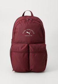 Bordo ruksak s dva prednja džepa na patent zatvaranje, bočnim mrežastim džepovima i logotipom koji glasi "PUMA ATHLETICS osnovan 1948." Tekstura tkanine.
