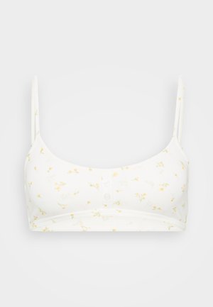 Bralette bianco con motivo floreale giallo, tessuto morbido, spalline regolabili e chiusura a bottone davanti. Tessuto liscio.