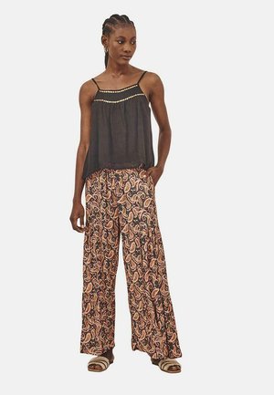 Top negro sin mangas con acentos de cuentas, combinado con pantalones de pierna ancha con estampado paisley en tonos naranjas y marrones. Sandalias planas.