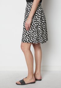 Jupe à motif noir et blanc avec une taille élastique, longueur genoux, fabriquée en tissu léger. Portée avec des sandales noires à glissière.