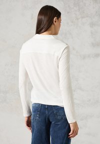 Lichtbeige langemouwen top met een ronde hals, gladde textuur en een rugpaneel detail. Gecombineerd met blauwe denim jeans.