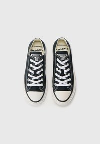 Black canvas low-top sneakers with white laces, rubber toe cap, and contrasting white stitching. Features “Converse” branding on the tongue.
