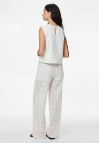 Haut sans manches en lin blanc avec un détail en trou de serrure au dos, associé à un pantalon blanc ample avec des motifs en œillet et une texture douce.
