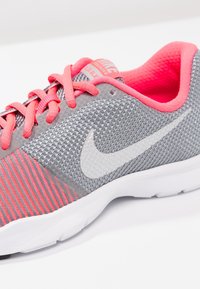 Šedá sportovní obuv Nike s růžovými akcenty. Disponuje síťovaným svrškem, texturovaným designem, bílým logem swoosh a polstrovaným límcem. Gumová podrážka.
