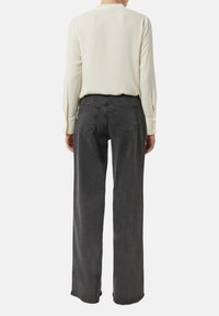 Jasnokremowa bluzka i spodnie dżinsowe w kolorze ciemnoszarym, o wysokim stanie i luźnym kroju, z pięciokieszeniowym wzorem oraz subtelnym przeszyciem na tylnych kieszeniach.