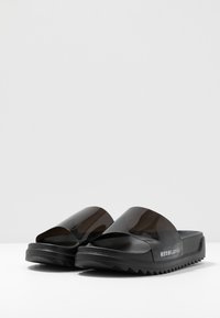 Sorte sandaler med en gennemsigtig overdel, tekstureret sål og takkede såler for bedre greb. Har japansk tekst på siden.