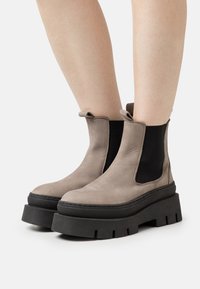 Botas de tobillo de ante beige con paneles laterales elásticos negros y gruesas suelas de plataforma negras. Cuentan con tiradores para facilitar su colocación.