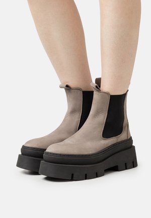 Botas de tobillo de ante beige con paneles laterales elásticos negros y gruesas suelas de plataforma negras. Cuentan con tiradores para facilitar su colocación.