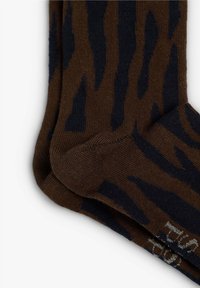 Calcetines marrones con un patrón de rayas de tigre azul, textura de punto, puntera y talón reforzados, y letras blancas cerca del puño.