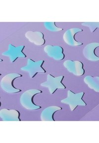 Autocollants brillants bleu pastel en forme d'étoiles, de lunes et de nuages disposés en rangées sur un fond violet.
