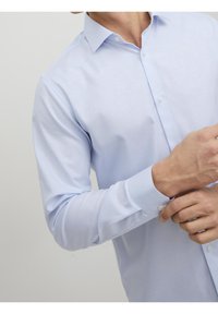 Jasnoniebieska koszula z długim rękawem z kołnierzykiem, zapinana na guziki z pojedynczymi mankietami na guziki. Gładki materiał i dopasowany krój są widoczne.