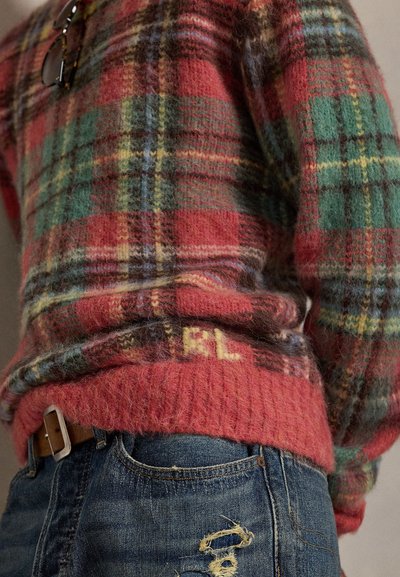 Flerfärgad rutig tröja med lös passform, i nyanser av rött, grönt och gult; mjuk textur och ribbad fåll; bärs med slitna blå jeans.