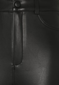 Svarta läderbyxor med en slät yta, som har knappstängning, framfickor och detaljerad sömnad längs sömmarna.