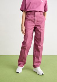 Roze op maat gemaakte broek van gladde stof, met een hoge taille, rechte pijpen en zijzakken, gecombineerd met witte sneakers.