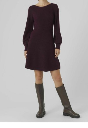Robe en tricot violet à manches longues et taille cintrée, s'évasant jusqu'à un ourlet au niveau du genou, associée à des bottes en cuir marron montant jusqu'aux genoux.