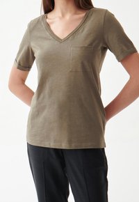 Oliwkowy t-shirt z krótkim rękawem i dekoltem w serek, z kieszonką na lewym piersi, oraz podwiniętymi mankietami; wykonany z miękkiego materiału.