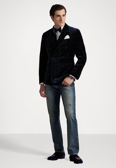 Blazer en velours à double boutonnage en écossais sombre, chemise blanche, nœud papillon bleu marine, jean bleu délavé et chaussures plates bleu marine avec détails brodés.