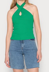 Gröna halterneck-top med korsade band och nyckelhålsdetalj; räfflad textur. Kombinerad med högmidjade denimshorts med något förstörd kant.