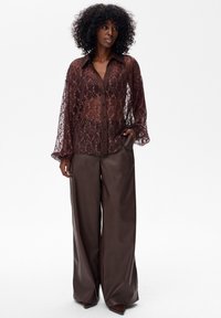 Koronkowa koszula z długim rękawem w głębokim burgundzie, z przezroczystym materiałem, w połączeniu z szerokimi spodniami z brązowej sztucznej skóry.